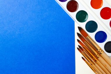 Suluboya boya kutusu ve mavi ve beyaz arka planda fırça seti