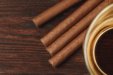 Bir bardak viski ve yuvarlanmış purolar ahşap masada.