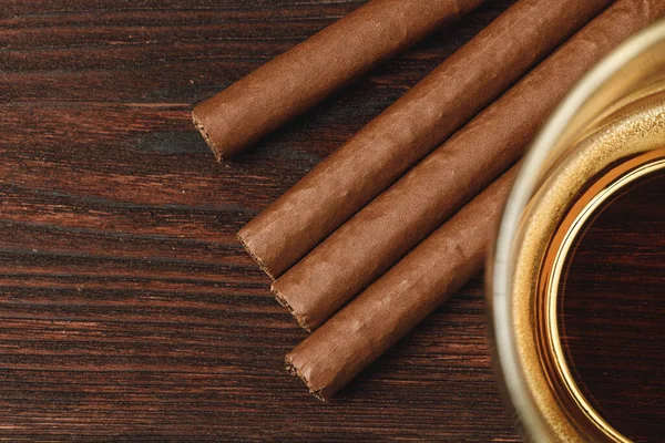 Bir bardak viski ve yuvarlanmış purolar ahşap masada.