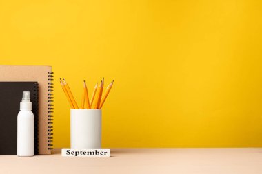 Masanın üzerinde sarı arka planda duran bir bardak kalem ve not defteri.