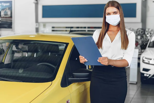 Woman car seller standing near new car wearing protective face mask