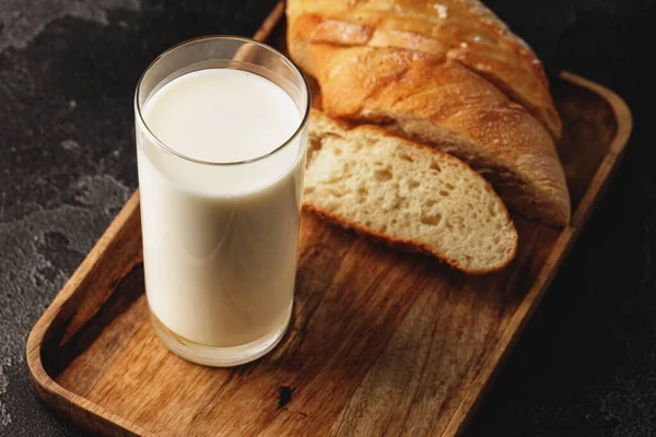 Egy pohár tejet szeletelt bagettel, fa táblán. — Stock Fotó
