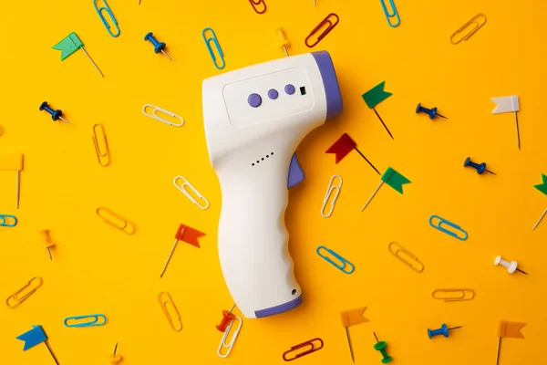 Non-contact infrared thermometer on yellow background. Concept of new schooling guidance after coronavirus lockdown