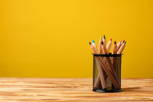 Office cup with pencils and stationery against yellow background