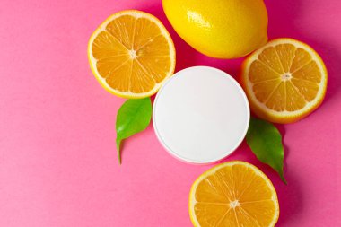 Parlak pembe arka planda dilimlenmiş narenciye meyveli kozmetik şişesi.