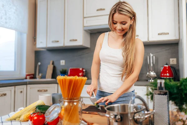 Sorrindo jovem cozinhando algo em sua cozinha — Fotografia de Stock