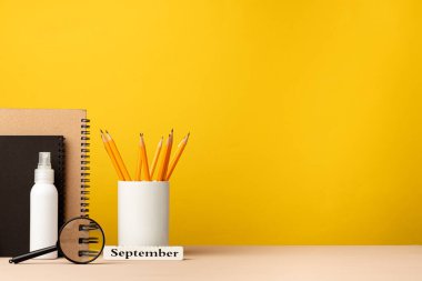 Masanın üzerinde sarı arka planda duran bir bardak kalem ve not defteri.