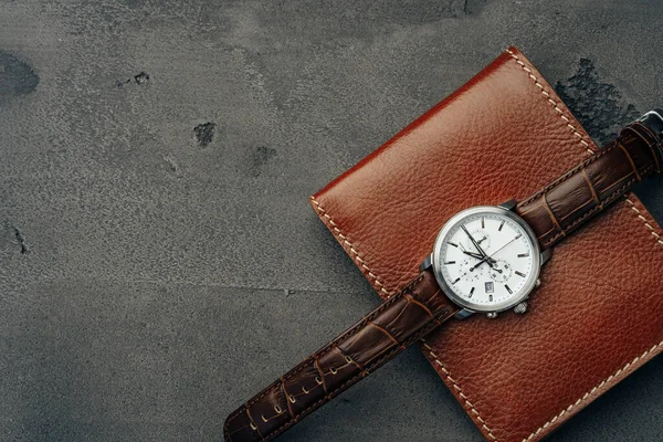 Male watch and leather wallet on dark grey surface