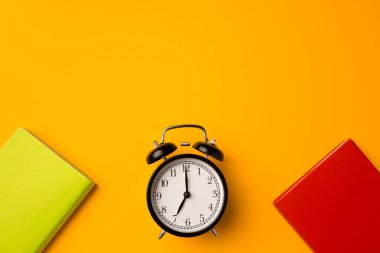 Sarı arka planda üç renkli hardcover defter ve alarm saati.