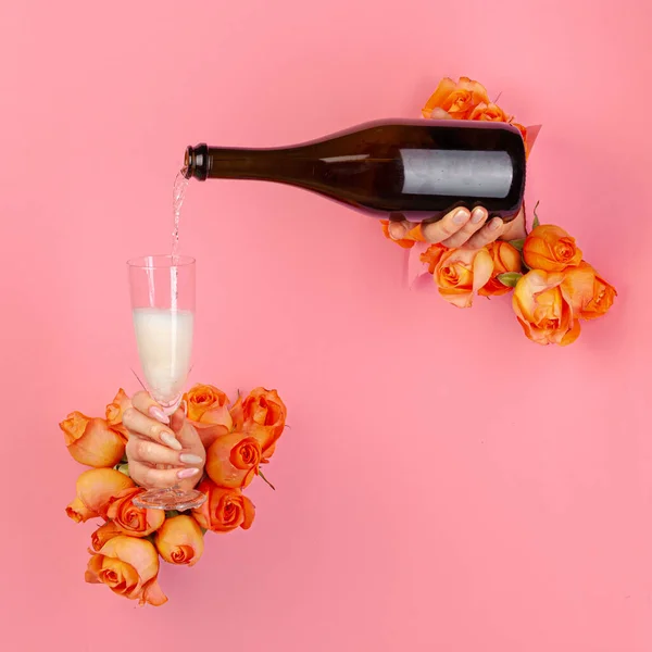 Mano femminile con manicure versando champagne in un bicchiere attraverso un buco in una carta strappata decorata con rose — Foto Stock