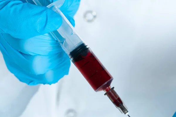 Doctor in blue gloves keep in hands test tube with a blood and syringe — Stock Photo, Image