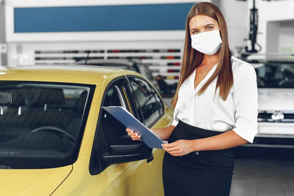 Woman car seller standing near new car wearing protective face mask