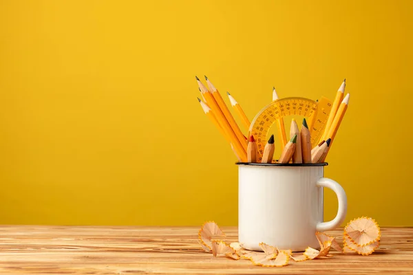 Metal cup with sharp pencils and pencil shavings on wooden desk