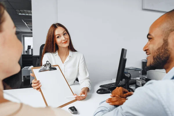 Junge Autoverkäuferin zeigt mehreren Autokäufern Vertrag — Stockfoto