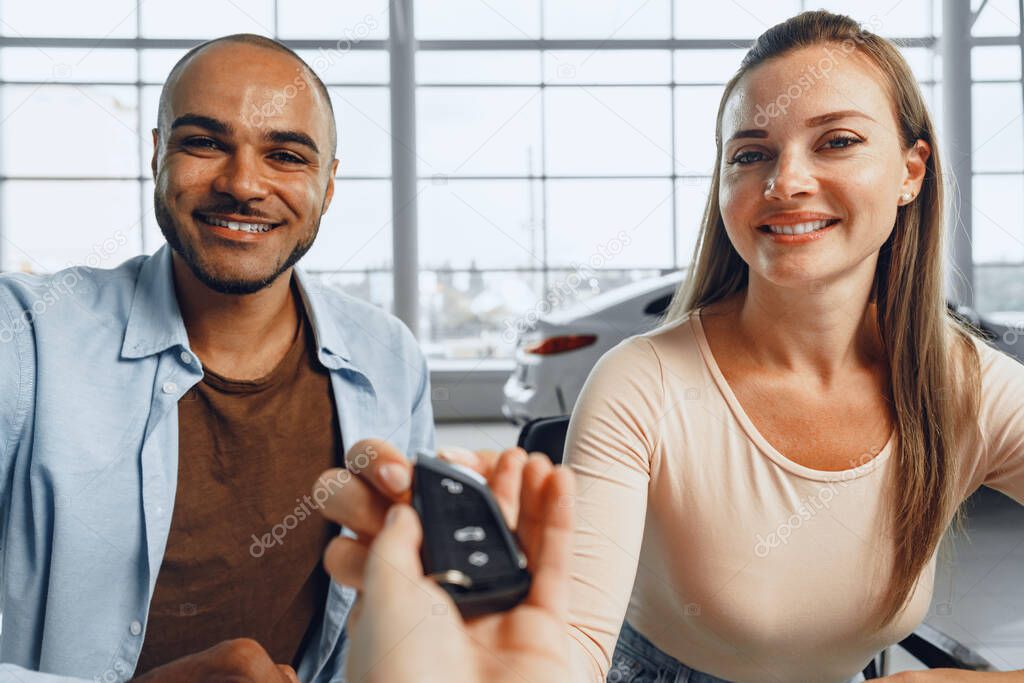 Cheerful couple taking keys of their new car in car dealership