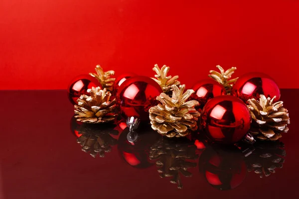 Rote Weihnachtskugeln und goldbemalte Kegel vor rotem Hintergrund — Stockfoto