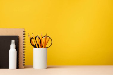 Masanın üzerinde sarı arka planda duran bir bardak kalem ve not defteri.