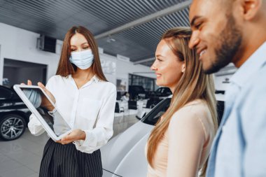 Tıbbi maske takan araba satıcısı, alıcılara dijital tablette bir şeyler gösteriyor.