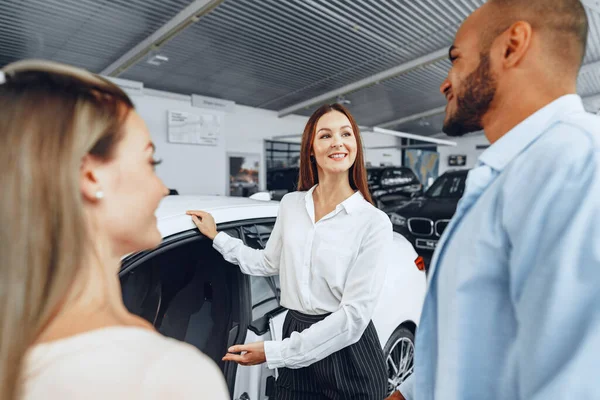 Mulher negociante de carro explicando aos compradores características de seu carro novo — Fotografia de Stock