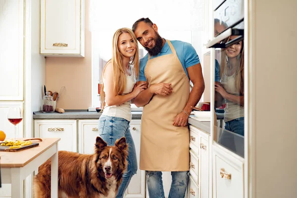 Casal feliz cozinhar comida na cozinha com seu cão — Fotografia de Stock