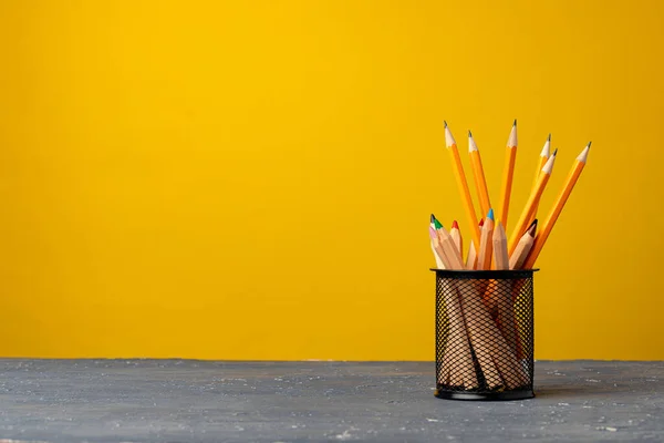 Офісна чашка з олівцями та канцелярськими приладами на жовтому тлі — стокове фото