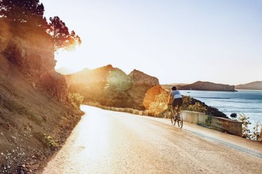 Bisikletli, sahil yolunda bisiklete biniyor.