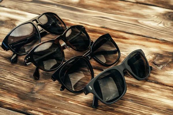 Set of dark sunglasses on brown wooden surface