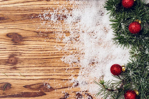 Placa de madeira com neve e bugigangas vermelhas de Natal — Fotografia de Stock