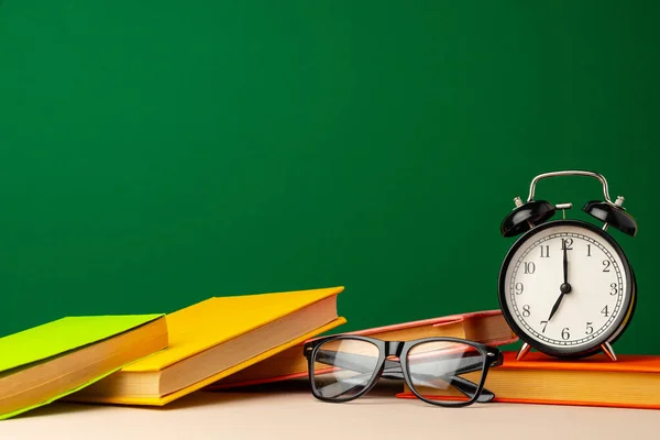 School supplies on wooden desk against green chalkboard