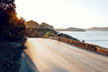 Bisikletli, sahil yolunda bisiklete biniyor.