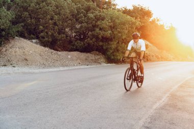 Bisikletli bir adam gün batımında açık havada bisiklet sürüyor.