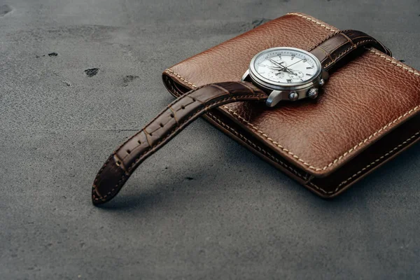 Male watch and leather wallet on dark grey surface