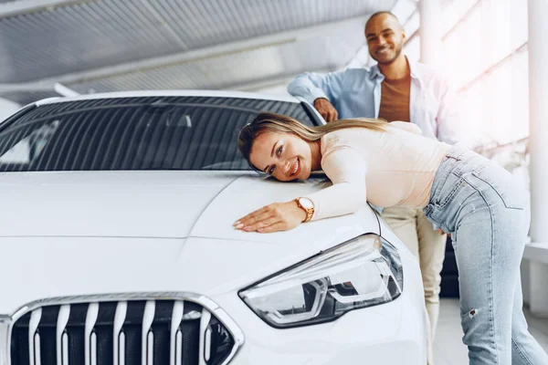 Junges Paar umarmt sein neues Auto in einem Autohaus — Stockfoto