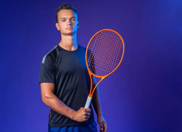 Caucasian young man tennis player posing with tennis racket against purple background