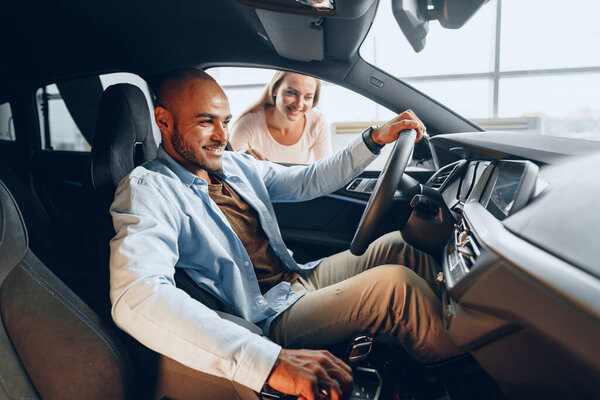 Joyful young couple looking around inside a new car they are going to buy in a car shop