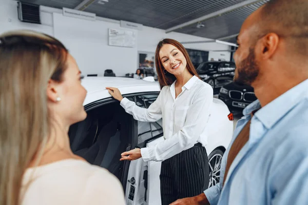 Mulher negociante de carro explicando aos compradores características de seu carro novo — Fotografia de Stock