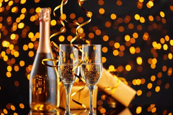 Botella de champán y regalo envuelto en fondo borroso de luces de Navidad — Foto de Stock