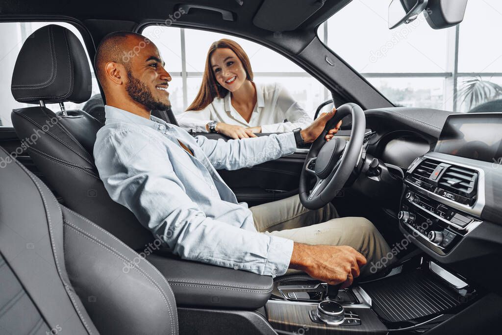 Young attractive woman salesperson in car showroom showing a car to her male client