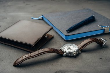 Koyu gri arka planda not defteri, saat ve çanta da dahil olmak üzere iş adamları aksesuarları