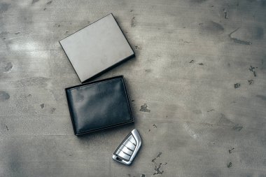 Koyu gri arka planda erkek deri cüzdanı ve araba anahtarı.