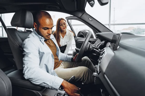 Joven vendedora atractiva en sala de exposición de coches mostrando un coche a su cliente masculino — Foto de Stock