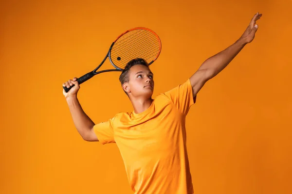 Estúdio tiro de um jovem jogador de tênis segurando raquete contra fundo laranja — Fotografia de Stock