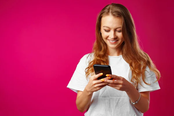 Fiatal mosolygós nő áll, és használja az okostelefon — Stock Fotó