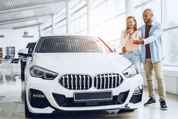 Jovem casal feliz escolhendo um carro na concessionária de carros — Fotografia de Stock