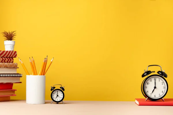 Tasse mit Bleistiften und Notizblöcken auf dem Schreibtisch vor gelbem Hintergrund — Stockfoto