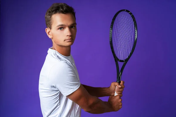 Caucasian young man tennis player posing with tennis racket against purple background