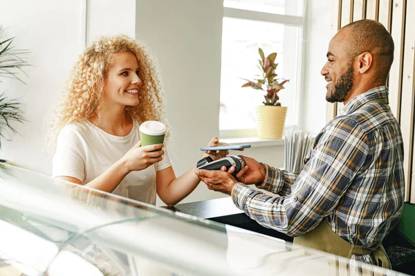 커피숍에서 커피를 사는 여성, 무선 전화를 통해 비접 촉식 기술을 이용 해 돈을 지불 한다 — 스톡 사진