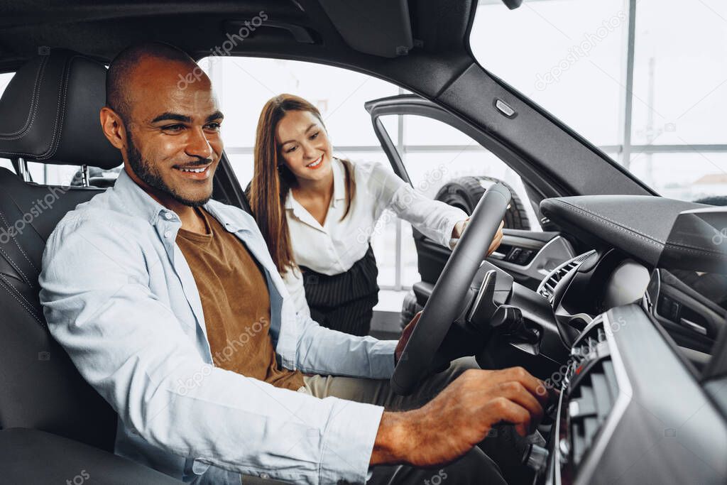 Young attractive woman salesperson in car showroom showing a car to her male client