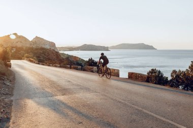Bisikletli, sahil yolunda bisiklete biniyor.
