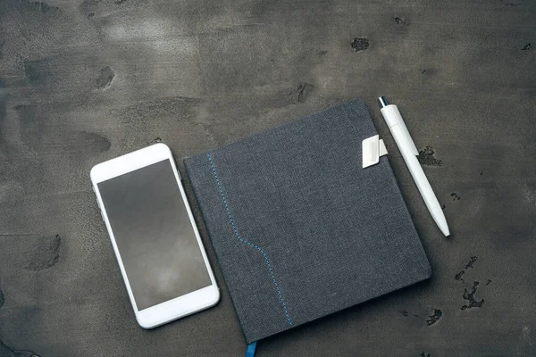 Blå anteckningsblock, smartphone och penna på mörkgrått bord — Stockfoto